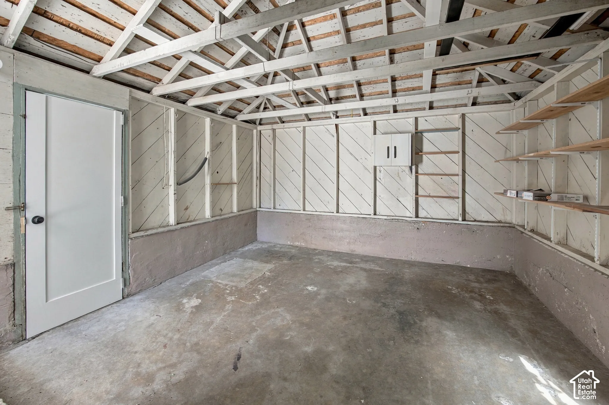 Exposed ceiling rafters, concrete flooring, built-in shelving, and a panel door with black hardware