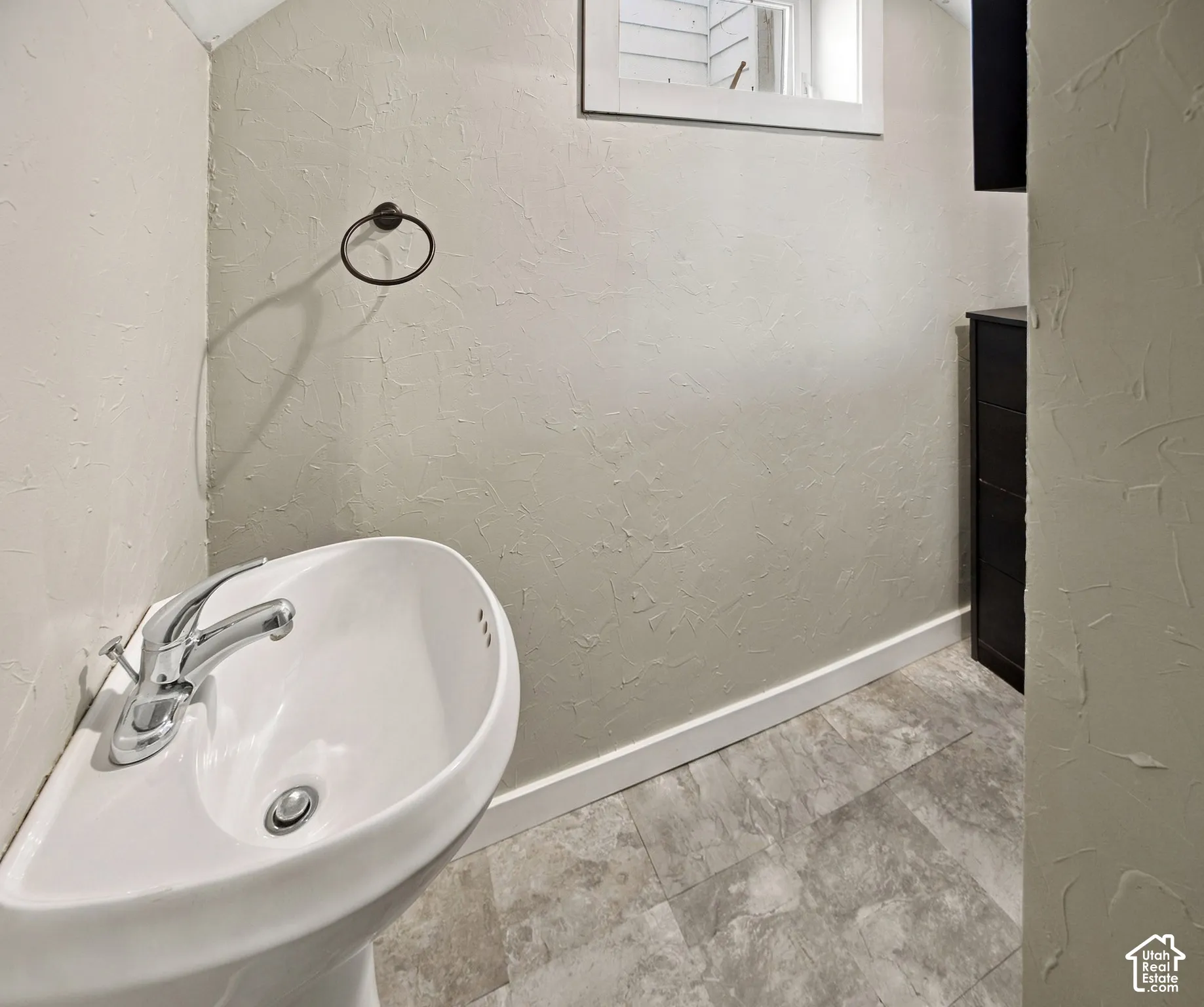 Pedestal sink with chrome faucet, textured wall finish, and tiled flooring