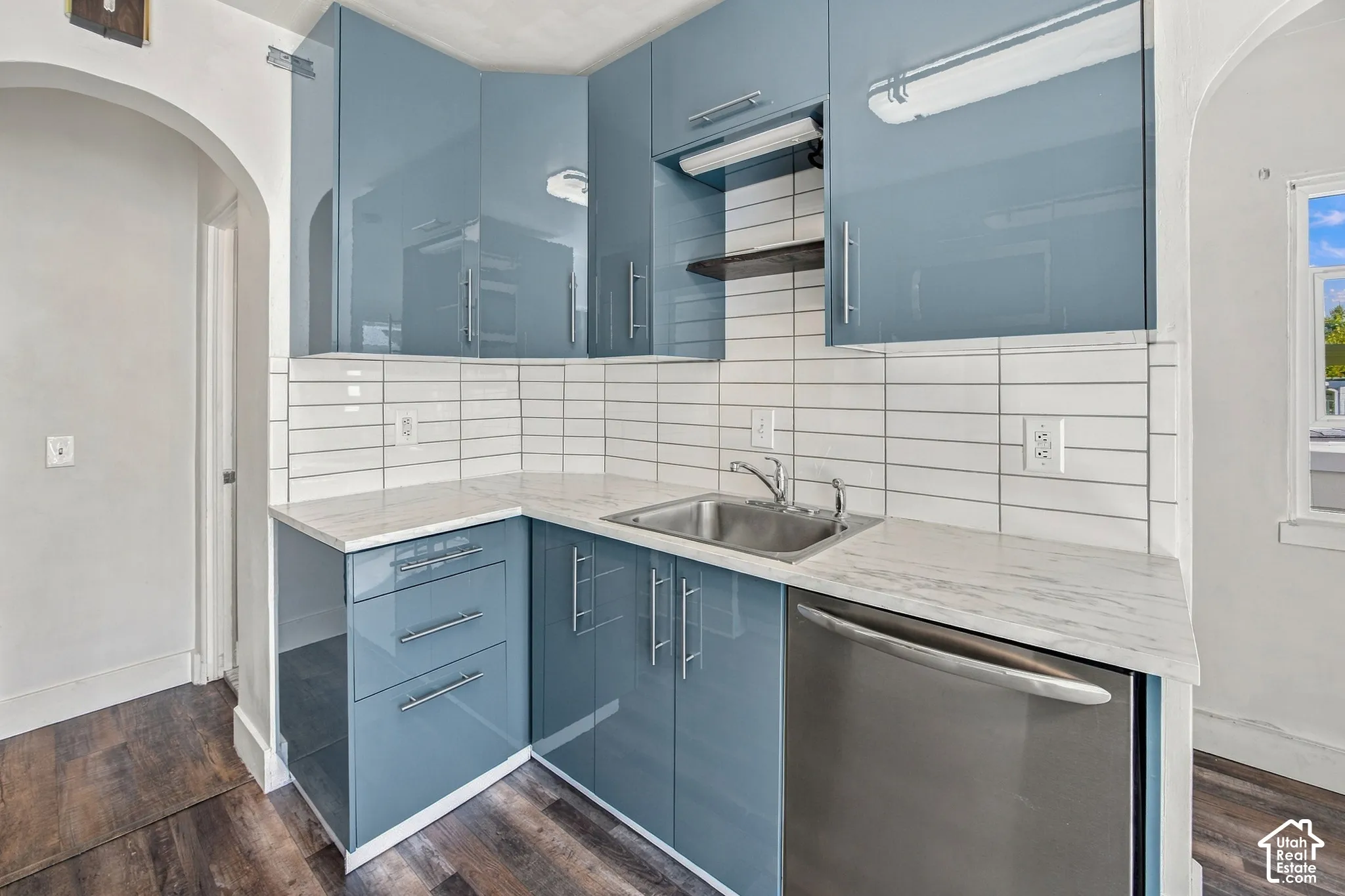 Light blue glossy cabinetry with stainless steel hardware, white rectangular tile backsplash, and a stainless steel sink