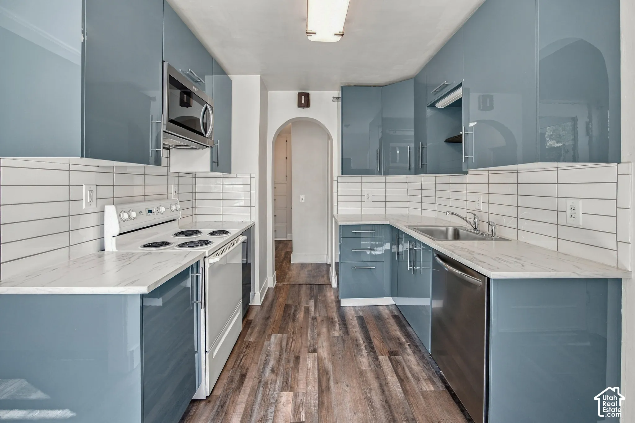 Galley kitchen featuring glossy blue cabinetry, white countertops, tile backsplash, and wood-finish flooring