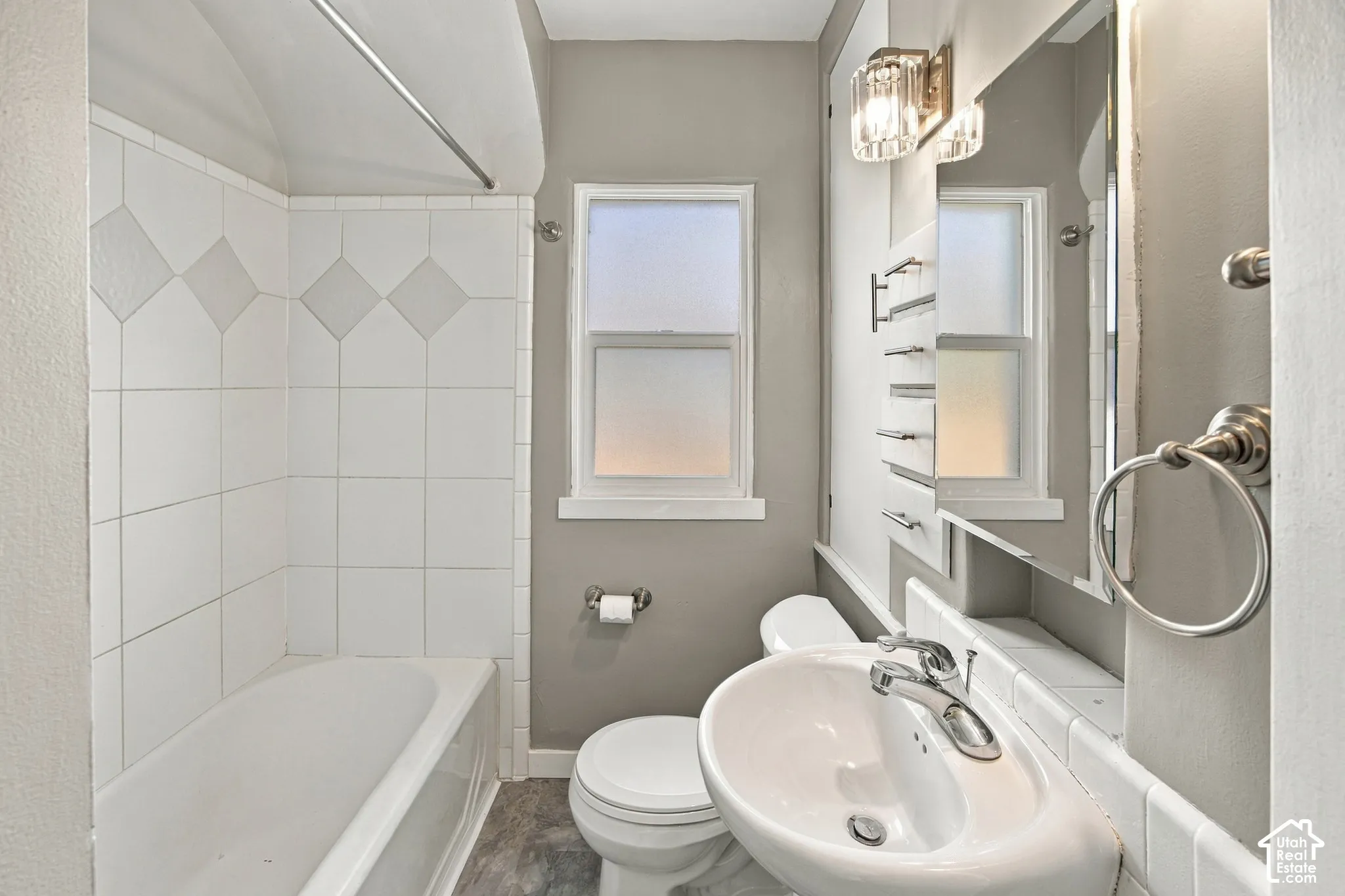 Bathroom featuring a pedestal sink, white subway tile shower surround with decorative accents, a window, and a wall-mounted light fixture