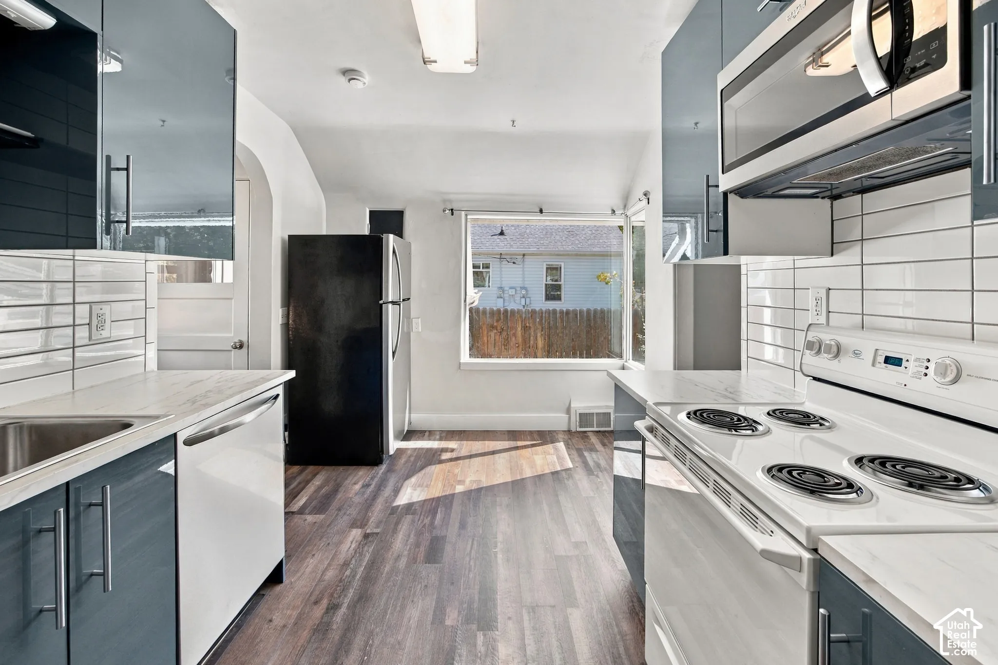 Kitchen featuring wood-finish flooring, white horizontal tile backsplash, stainless steel microwave, white electric range, and ample natural light