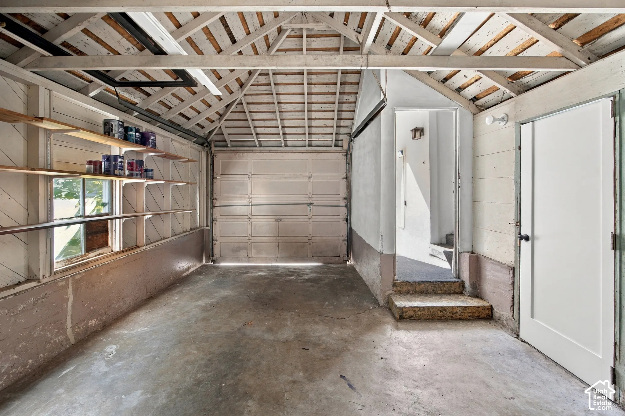Spacious garage featuring a concrete floor, built-in shelving, and a pedestrian door for interior access
