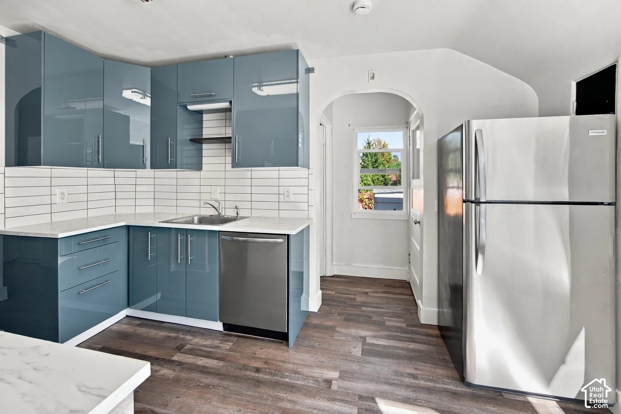 Kitchen featuring glossy blue cabinetry, white subway tile backsplash, white countertops, wood-finish flooring, and a stainless steel refrigerator