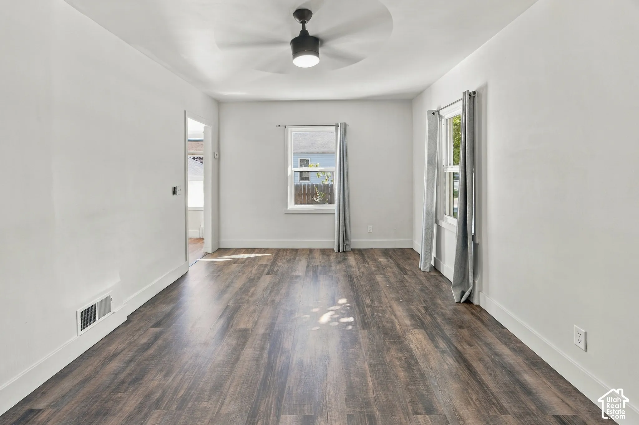 Wood-finish flooring throughout, white walls, black ceiling fan, and multiple windows