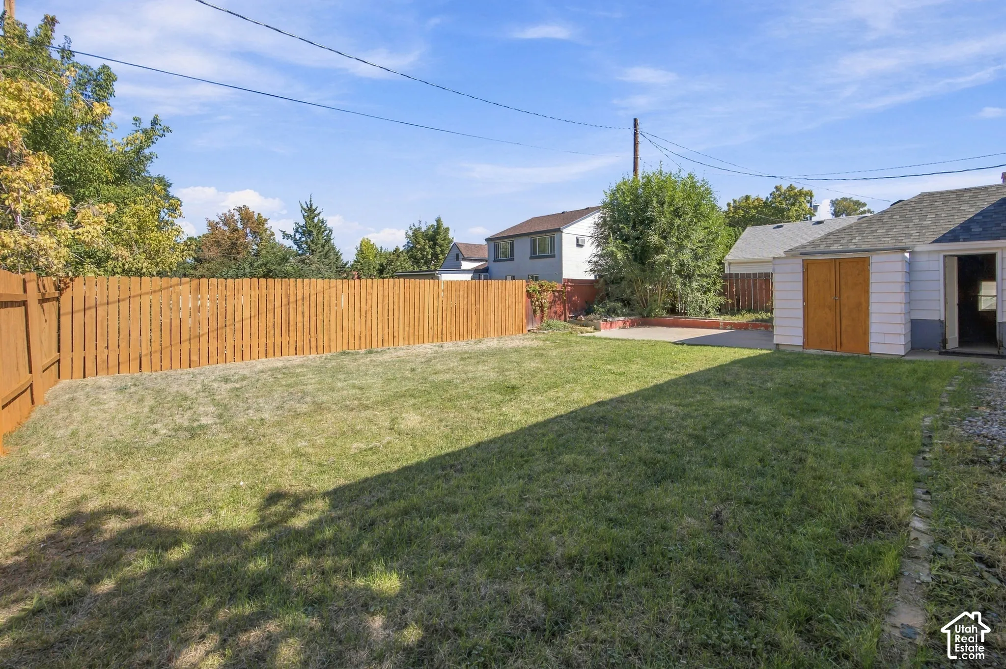 Expansive backyard featuring a natural wood privacy fence, a concrete patio, and a dedicated storage shed with wood doors
