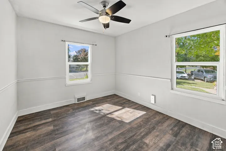 Wood-finish flooring, two large windows, chair rail molding, and a ceiling fan with integrated lighting