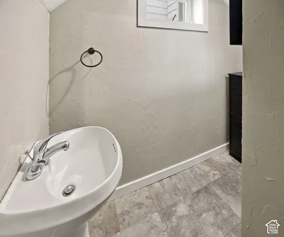 Pedestal sink with chrome faucet, textured wall finish, and tiled flooring