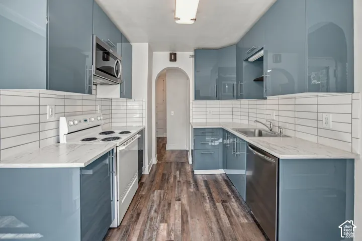 Galley kitchen featuring glossy blue cabinetry, white countertops, tile backsplash, and wood-finish flooring
