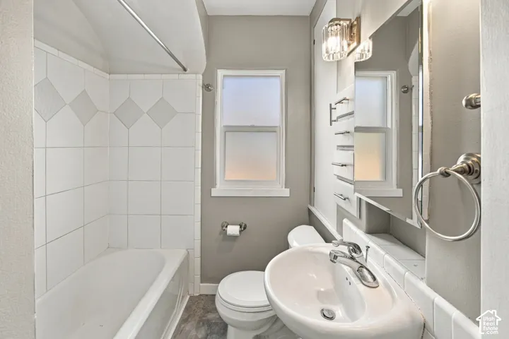 Bathroom featuring a pedestal sink, white subway tile shower surround with decorative accents, a window, and a wall-mounted light fixture