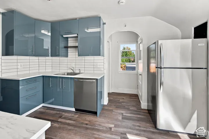 Kitchen featuring glossy blue cabinetry, white subway tile backsplash, white countertops, wood-finish flooring, and a stainless steel refrigerator