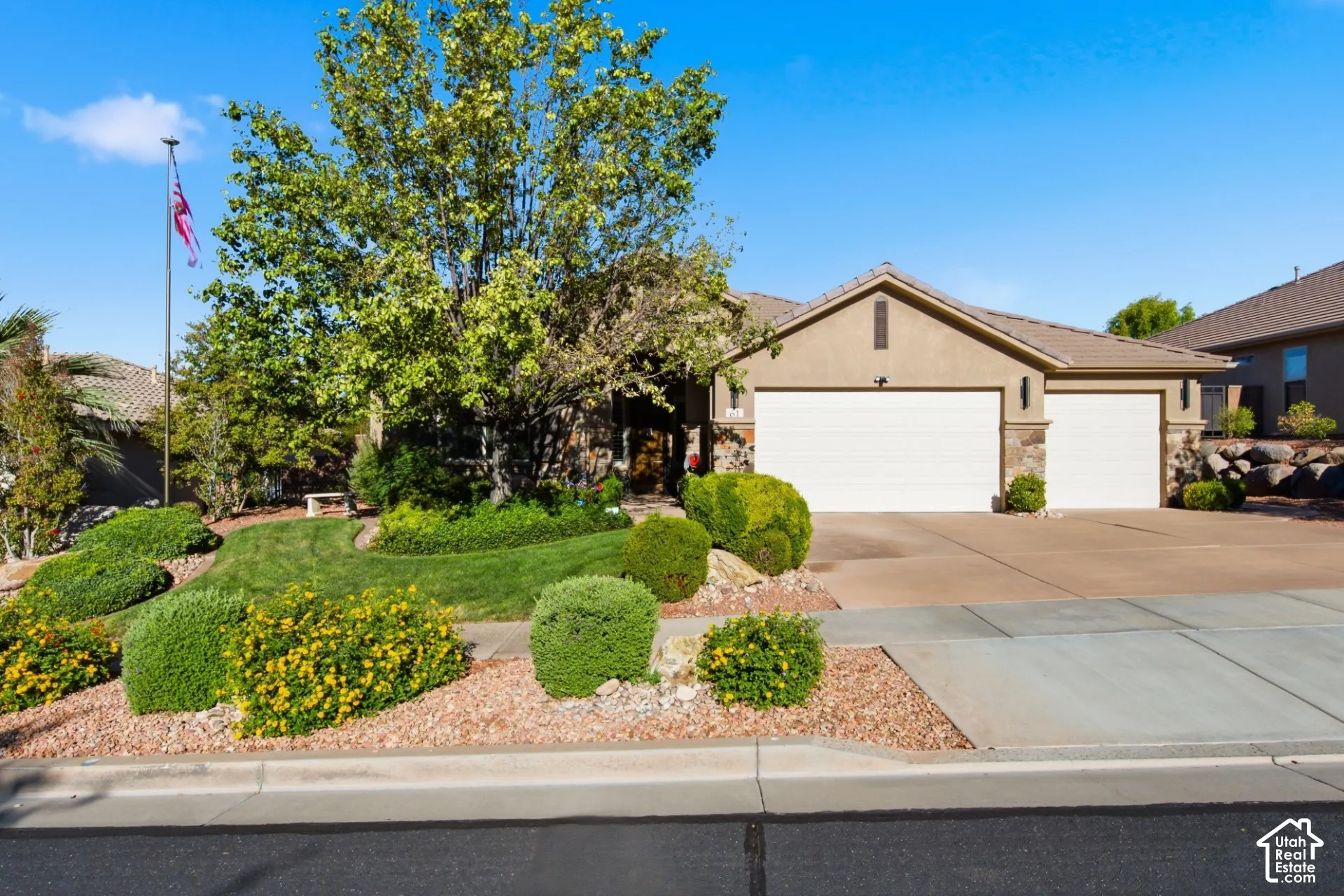 Stucco exterior with stone accents, concrete tile roof, two-car garage, and mature landscaping