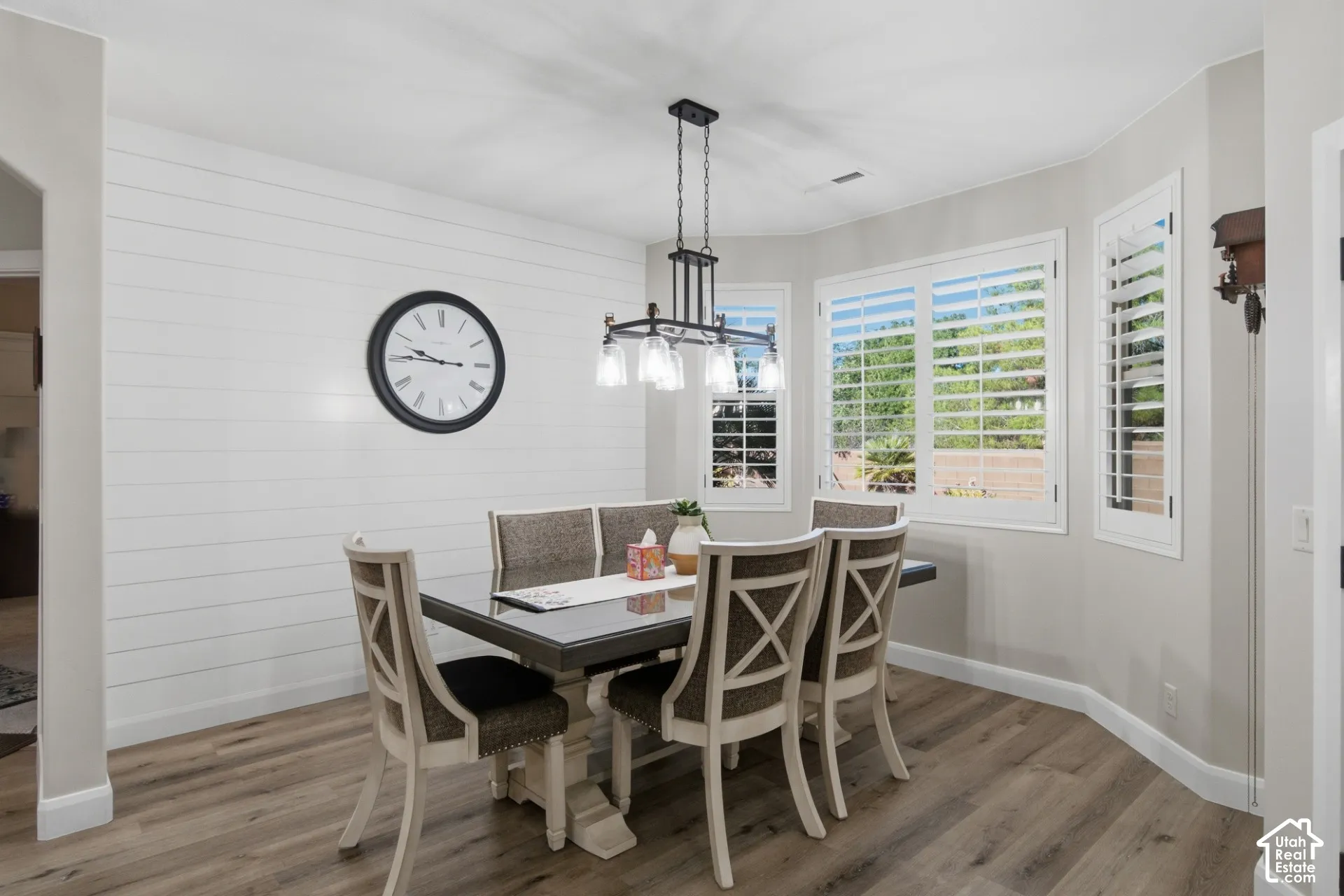 Wood-finish flooring, accent shiplap wall, multiple windows with plantation shutters, and a suspended chandelier