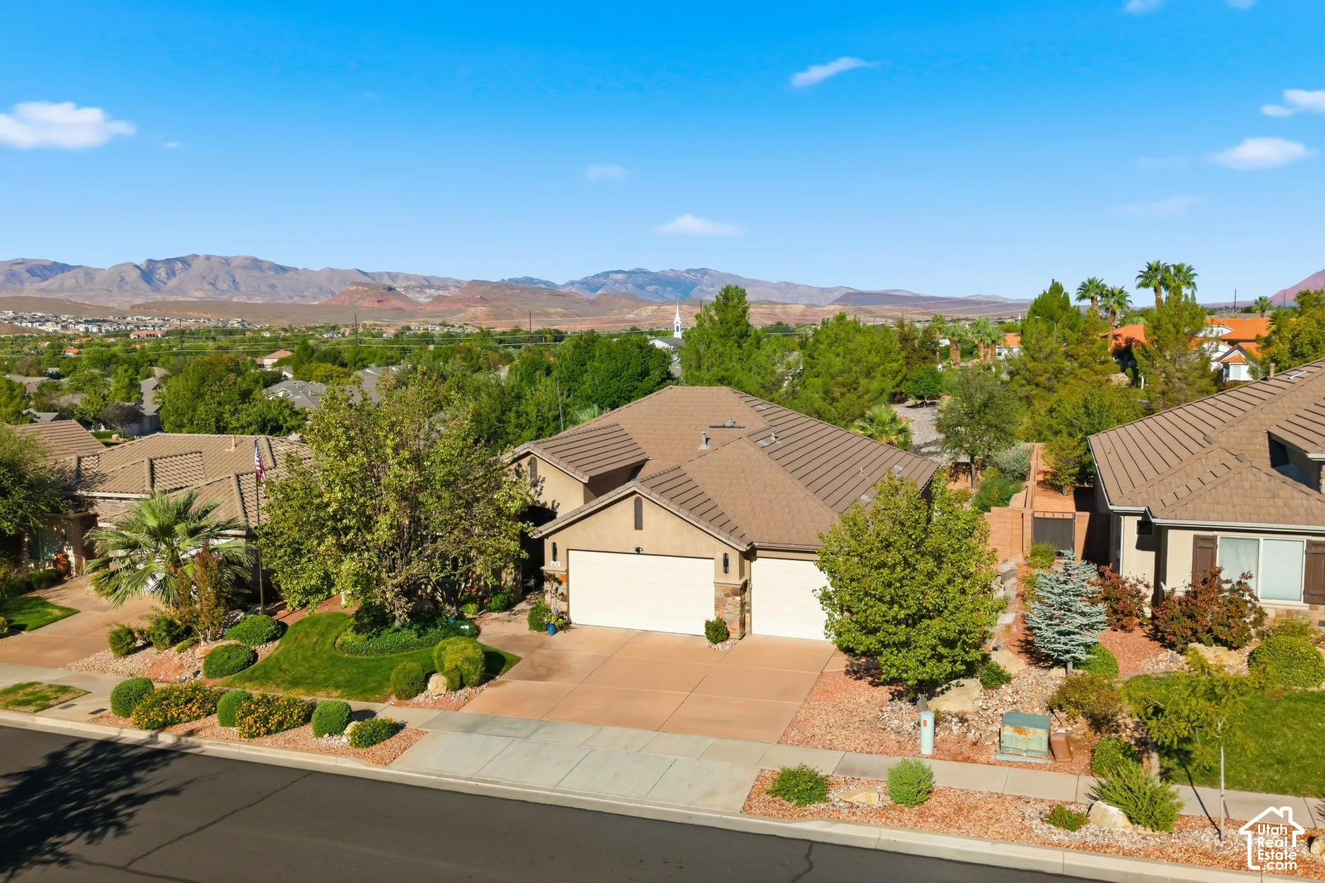 Terracotta roof tiles, light stucco exterior, two-car garage, mature landscaping, and a paved driveway