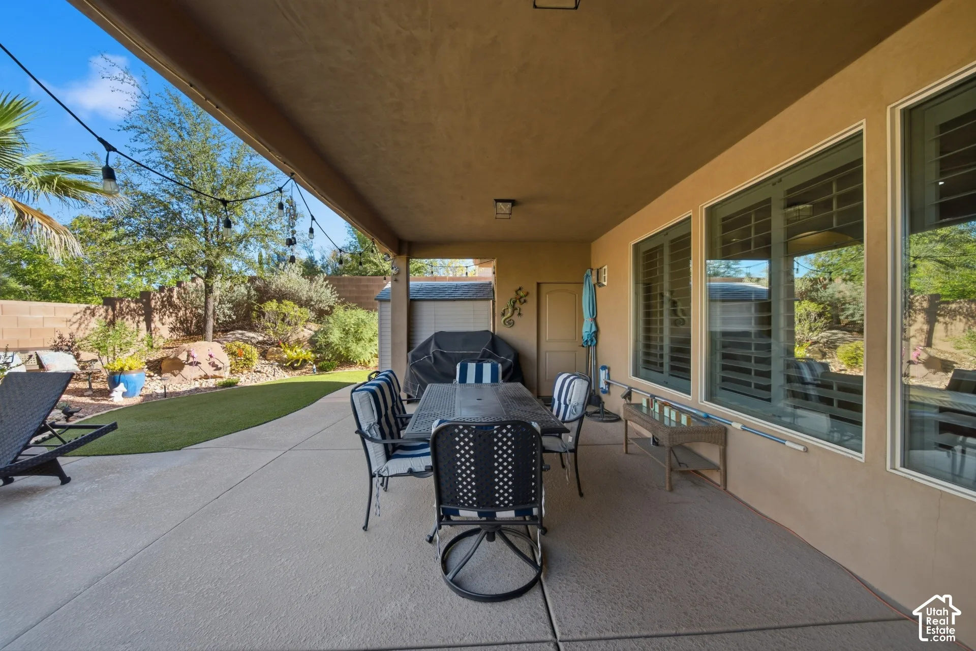 Covered patio with concrete flooring, multiple windows with internal blinds, and string lighting