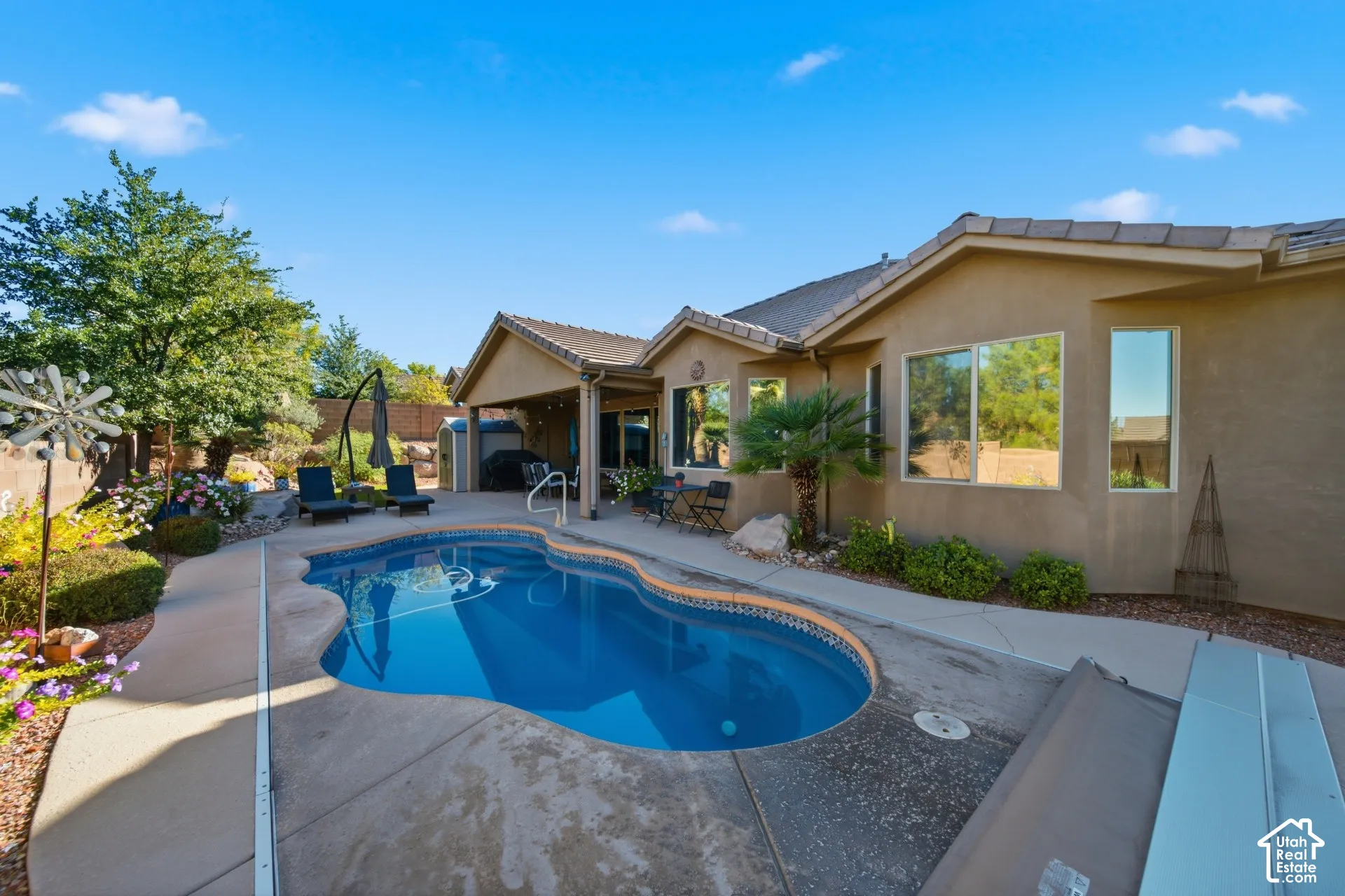 Landscaped backyard featuring a freeform swimming pool, concrete patio, and covered outdoor living area