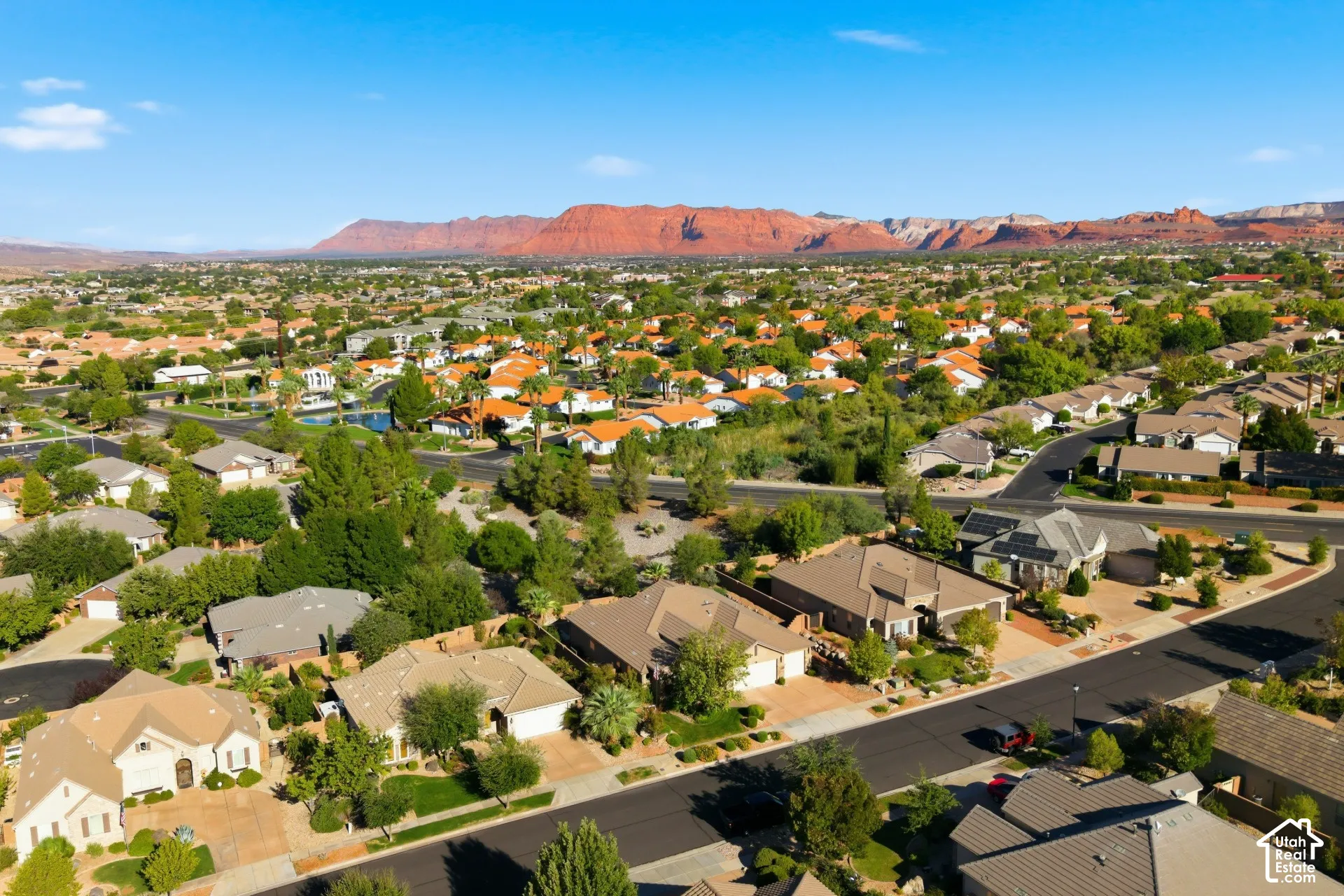Residential neighborhood with mature trees, surrounded by distant red rock formations