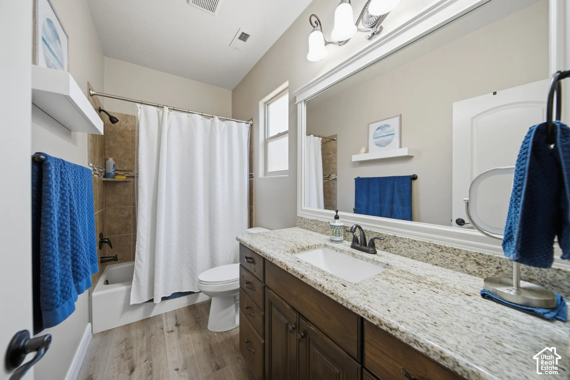 Wood-finish plank flooring, a single vanity with stone countertop, a rectangular undermount sink, and dark bronze fixtures define this bathroom