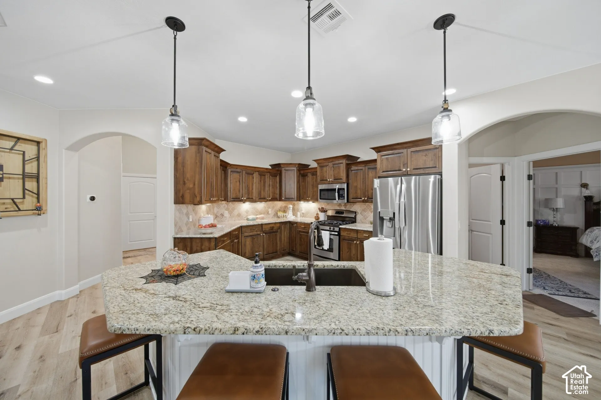 Kitchen featuring wood-finish cabinetry, stainless steel appliances, and a central island with a sink and stone countertop