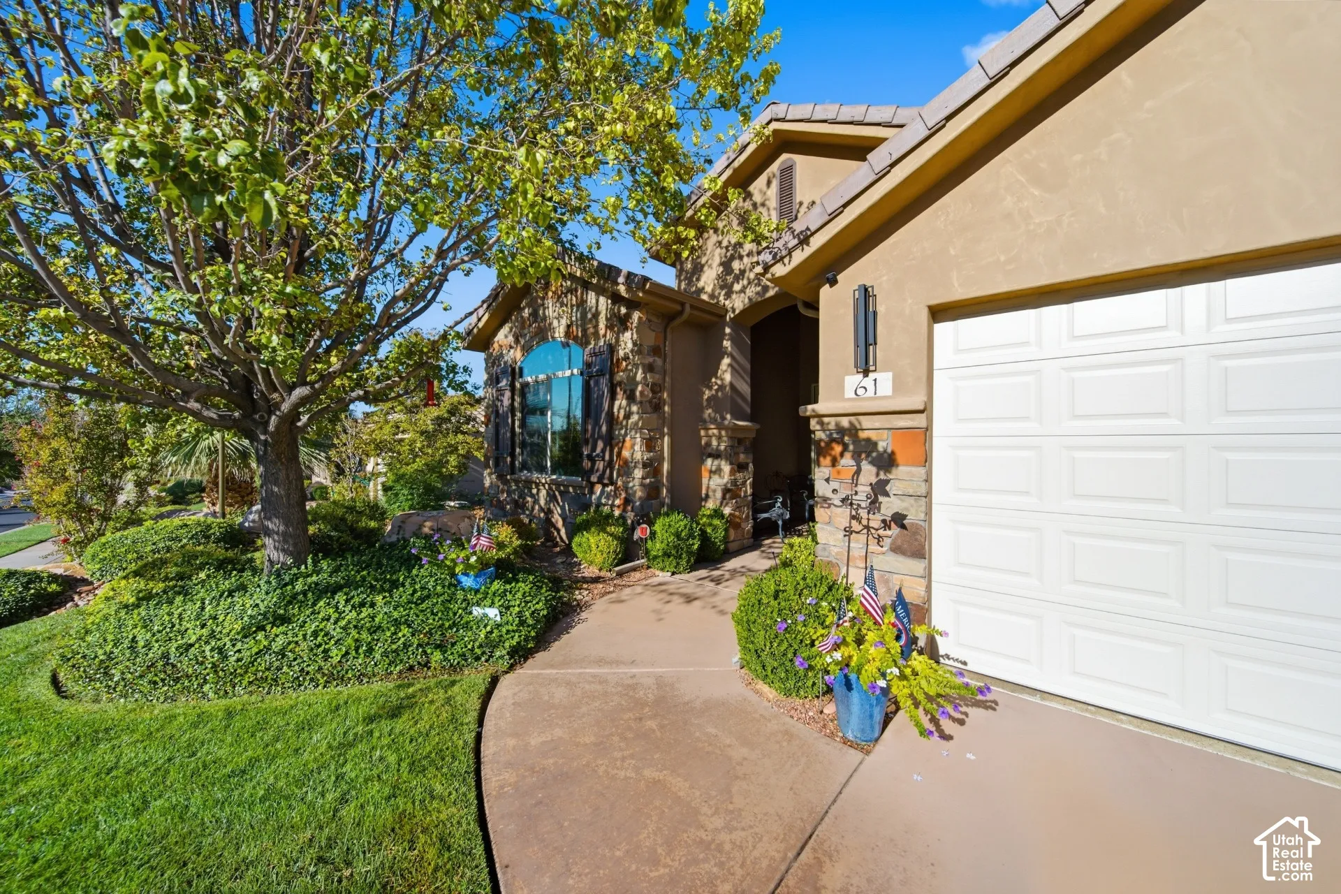 Stucco exterior with stone accents, arched window with shutters, concrete pathway, and a paneled garage door