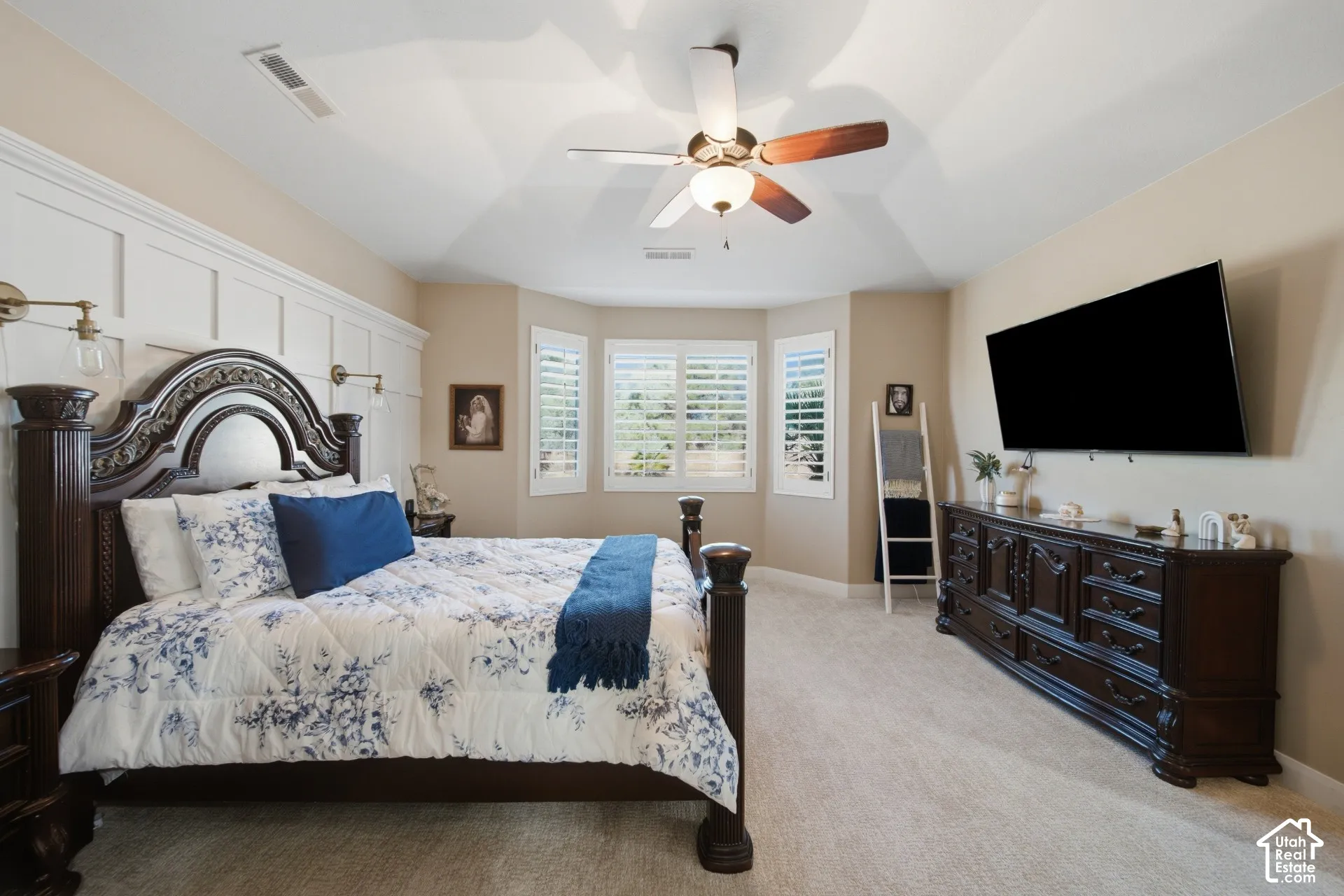 Tray ceiling with a ceiling fan, wall-mounted sconces, and paneling detailing on the wall
