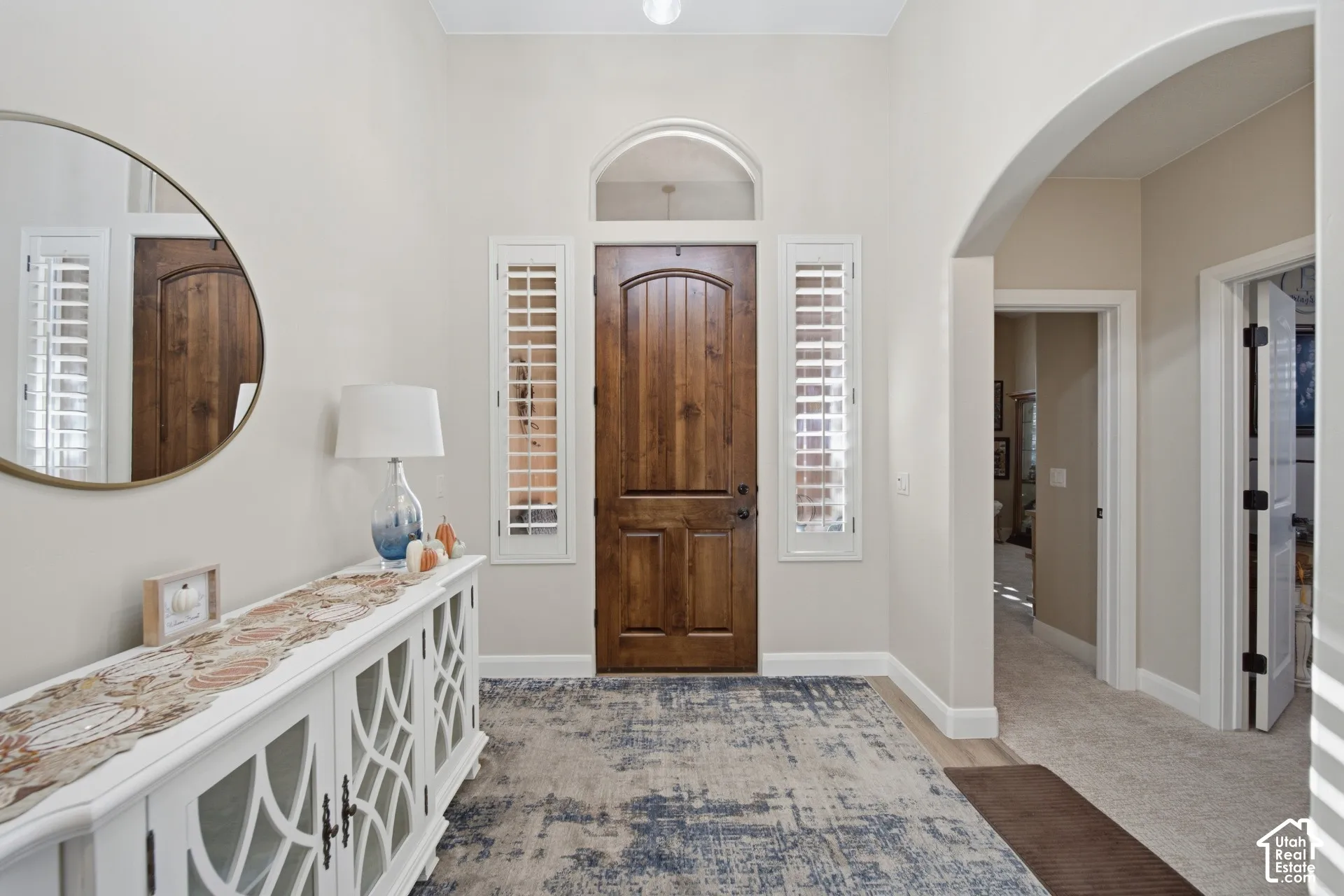 Arched entry, wood-paneled door, sidelight windows with plantation shutters, overhead lighting, and neutral wall tones