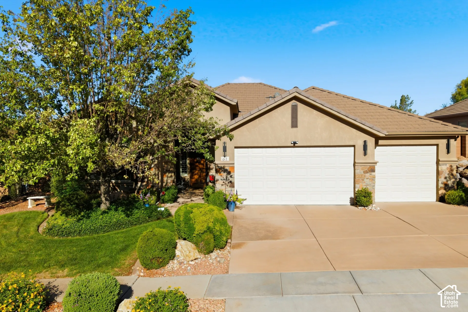 Stucco exterior with stone accents, a multi-car garage, concrete driveway, and mature landscaping