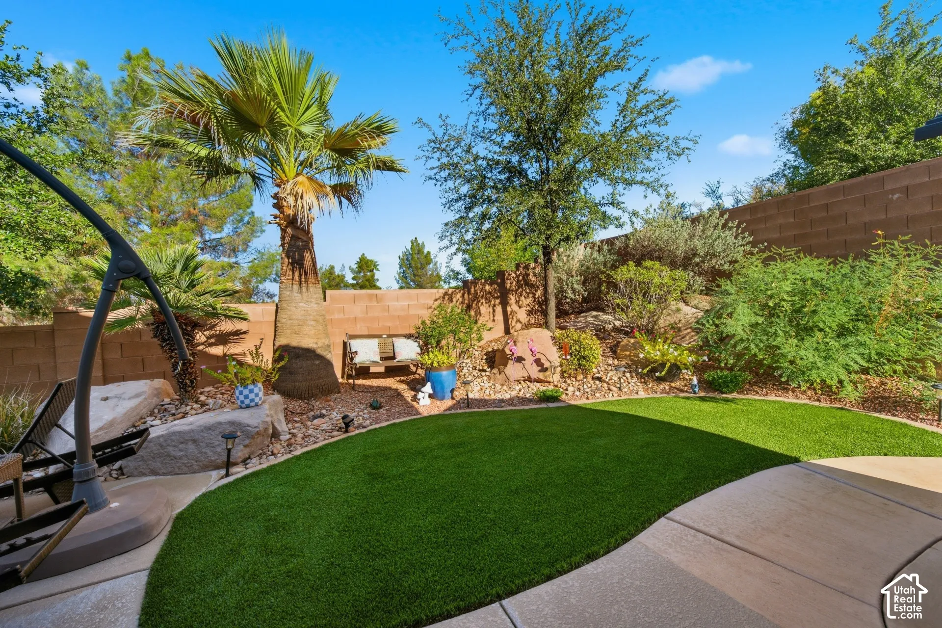 Expansive backyard featuring a manicured artificial lawn, mature palm trees, terraced landscaping with desert-adapted plantings, and a block wall perimeter