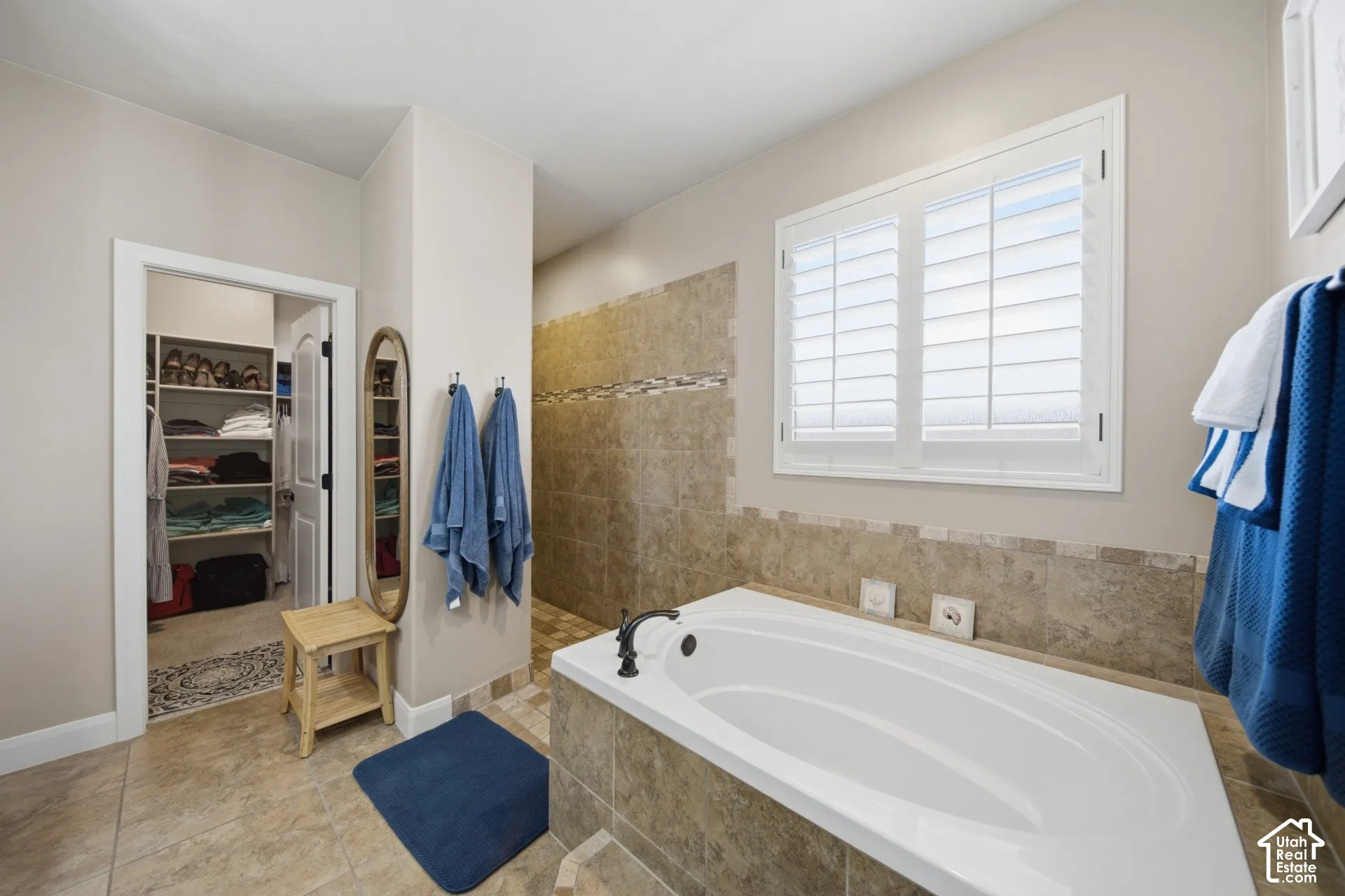 Built-in soaking tub, tiled shower with mosaic accent, built-in closet shelving, window with plantation shutters, and tiled flooring