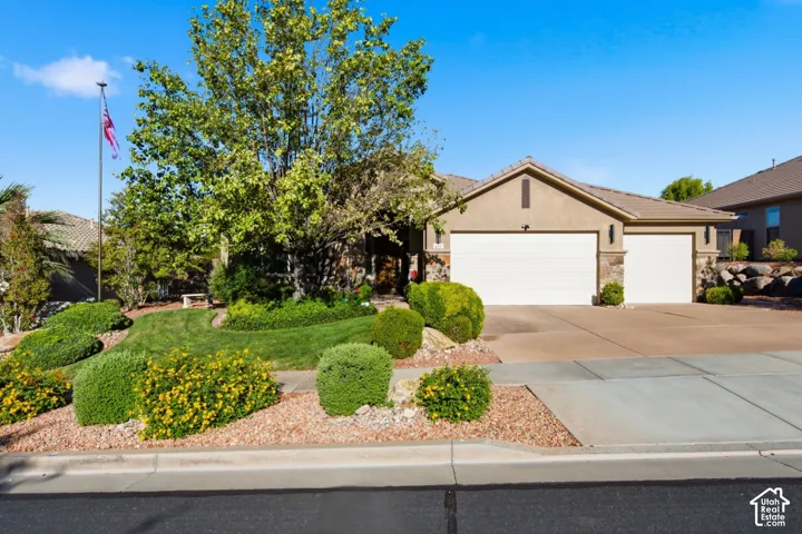 Stucco exterior with stone accents, concrete tile roof, two-car garage, and mature landscaping