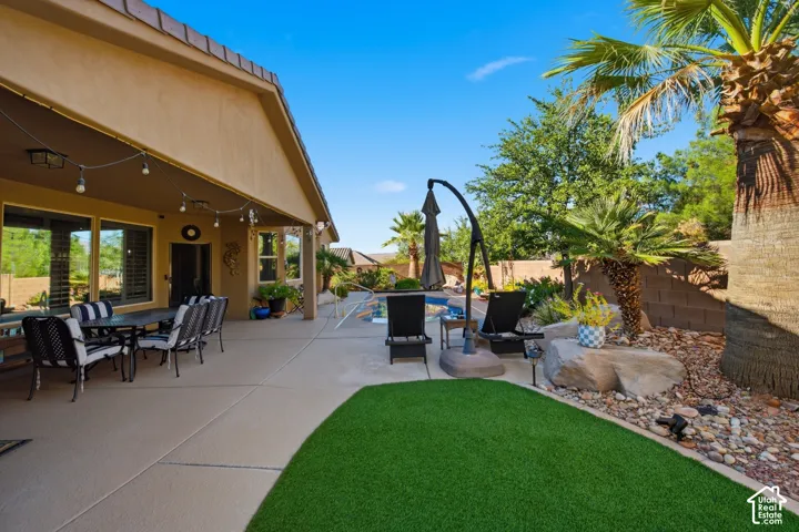 Expansive patio featuring a covered dining area, artificial turf, mature palm trees, and a rock garden