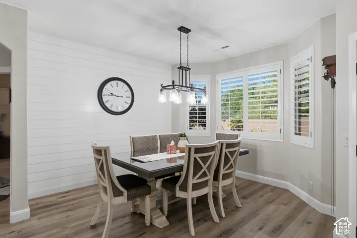 Wood-finish flooring, accent shiplap wall, multiple windows with plantation shutters, and a suspended chandelier