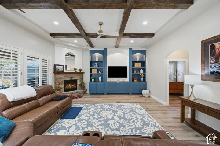 Vaulted ceiling with wood beams, recessed lighting, stone fireplace, built-in media cabinetry, and wood-finish flooring
