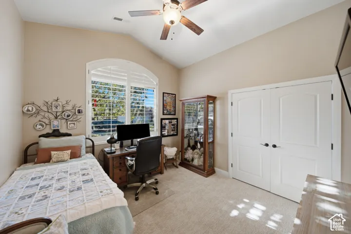 Vaulted ceiling with a ceiling fan, arched window with plantation shutters, double closet doors, wood-finish desk, and carpeting
