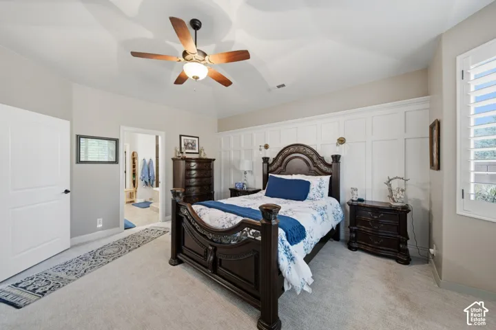 Vaulted ceiling with a ceiling fan, accent wall with paneling, window with plantation shutters, light neutral wall color, and carpet flooring