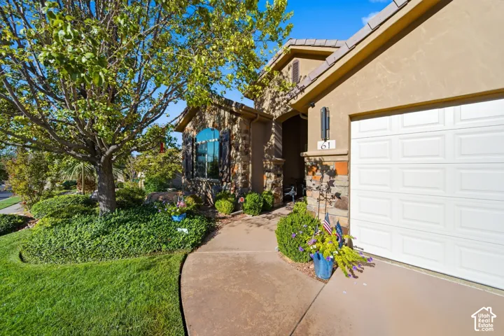 Stucco exterior with stone accents, arched window with shutters, concrete pathway, and a paneled garage door