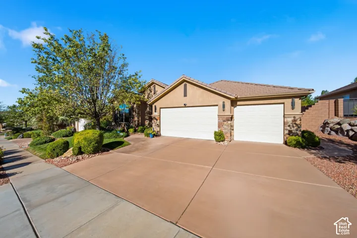 Stucco exterior with stone accents, two-car garage, concrete driveway, and established landscaping