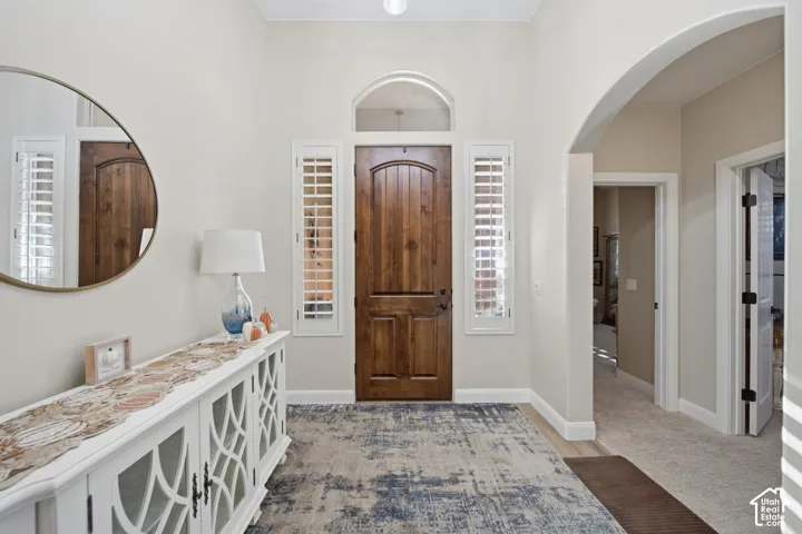 Arched entry, wood-paneled door, sidelight windows with plantation shutters, overhead lighting, and neutral wall tones