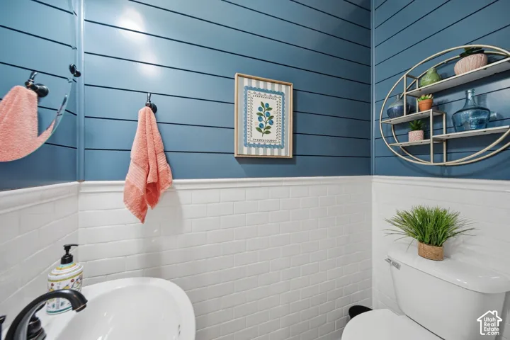 White subway tile wainscoting, blue shiplap walls, wall-mounted mirror, white pedestal sink with dark finish faucet, and white toilet