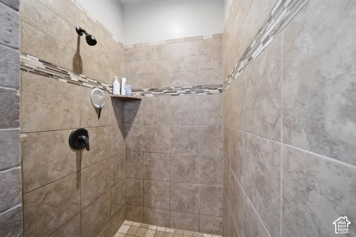 Tiled shower enclosure featuring a dark-finish shower head and control, a decorative mosaic tile accent band, and a built-in corner shelf