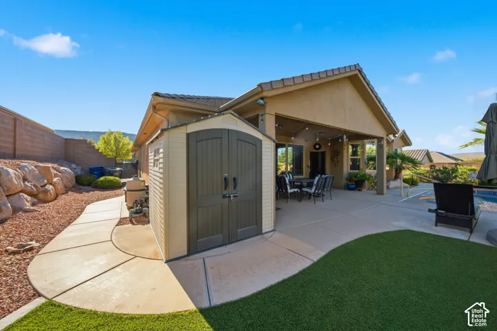 Expansive concrete patio with covered outdoor dining area, artificial turf lawn, and a storage shed