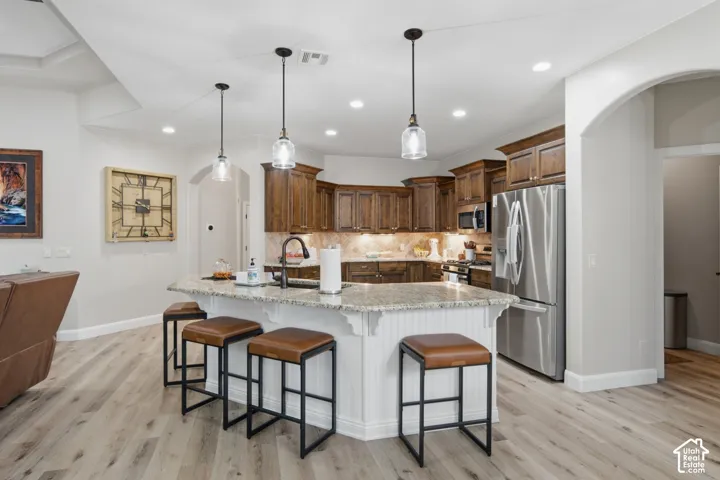 Kitchen island with pendant lighting, granite countertop, wood-finish flooring, stainless steel appliances, and wood cabinetry