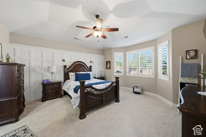 Tray ceiling with a ceiling fan, accent wall with wainscoting, and multiple windows with plantation shutters