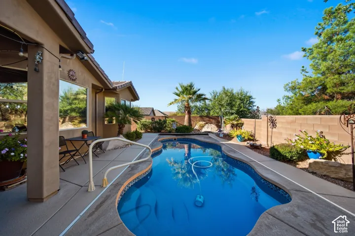 Private outdoor oasis featuring a freeform swimming pool, concrete hardscaping, stucco exterior, and a block wall perimeter