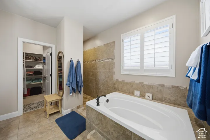 Built-in soaking tub, tiled shower with mosaic accent, built-in closet shelving, window with plantation shutters, and tiled flooring