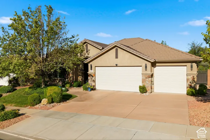 Stucco exterior with stone accents, concrete driveway, two garage doors, and mature landscaping