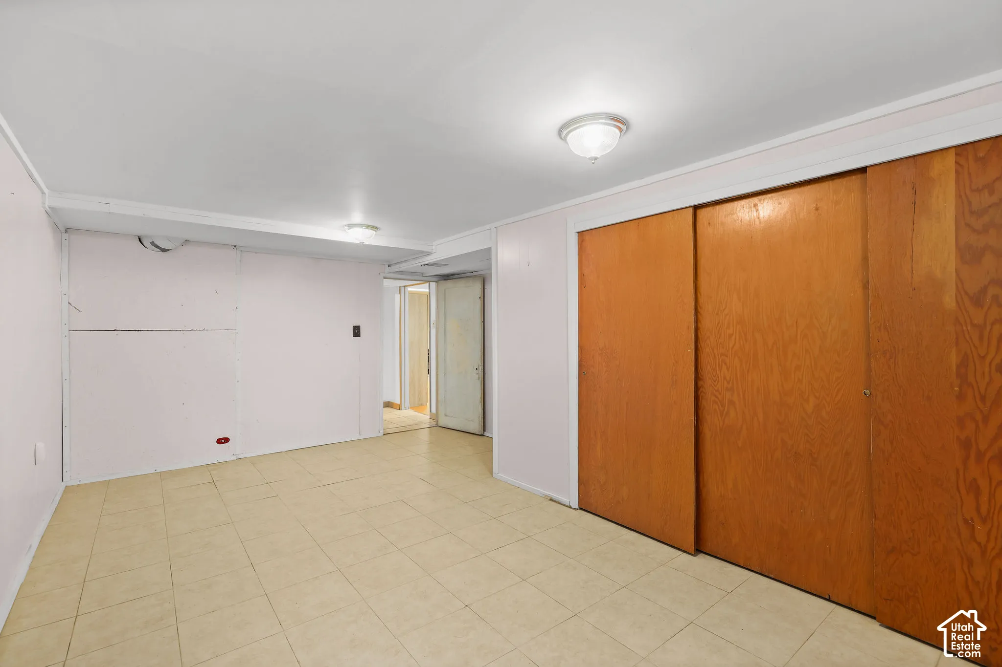 Spacious room featuring neutral-toned tile flooring, white walls, and a built-in wardrobe with wood-finish sliding doors