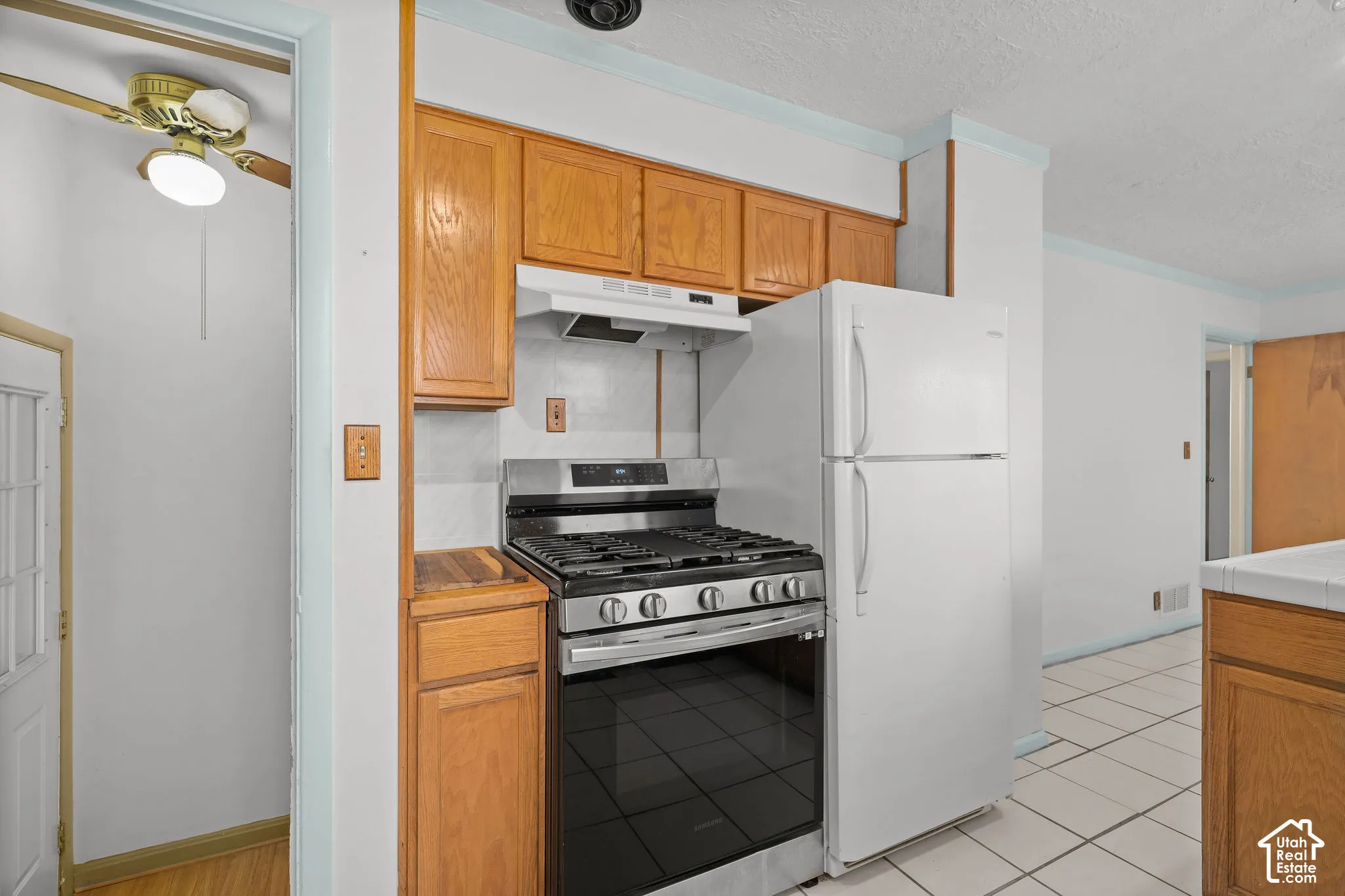 Kitchen featuring wood-finish cabinetry, stainless steel range, white refrigerator, and white tile flooring