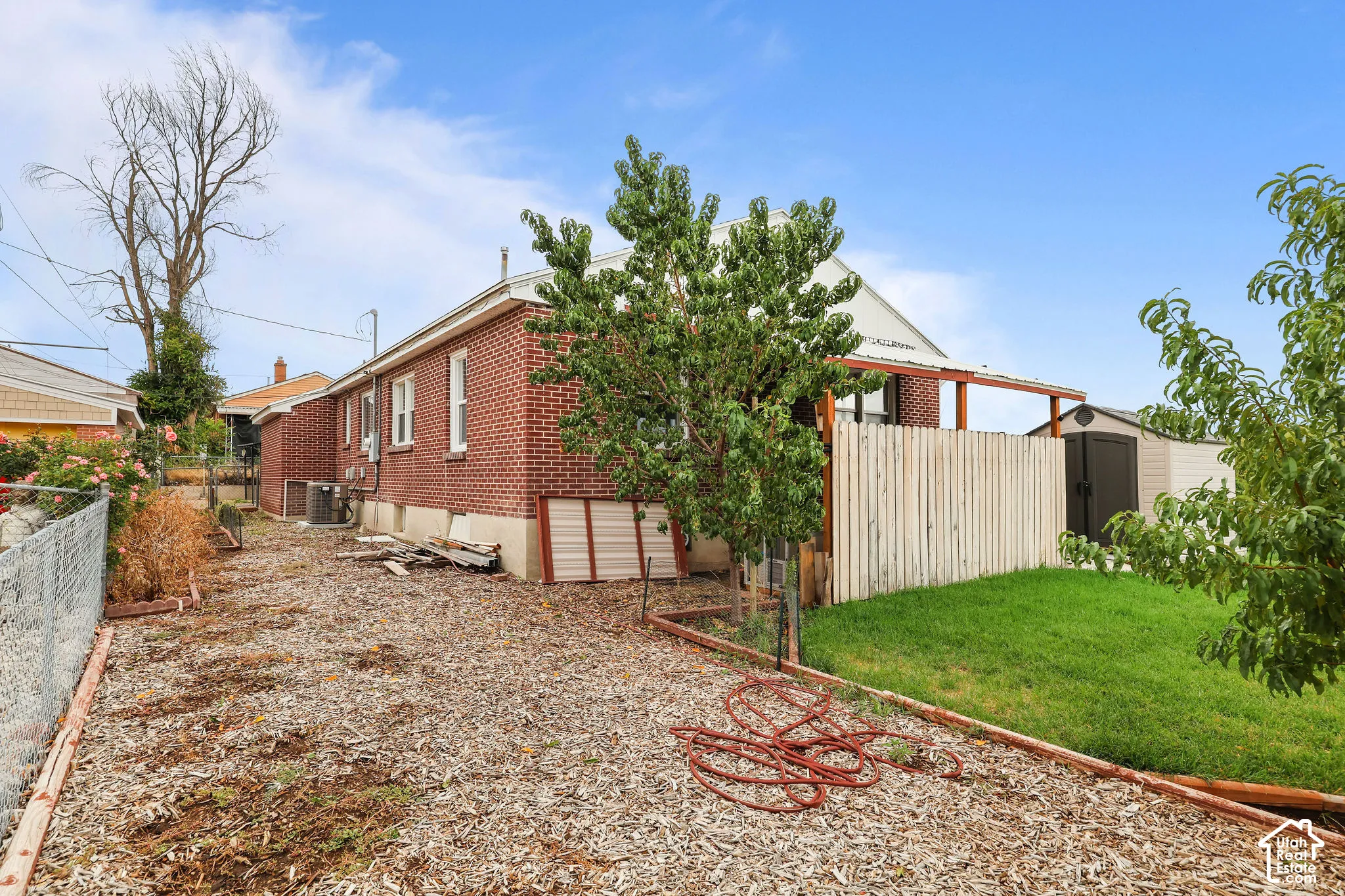 Brick exterior with a covered patio structure, a privacy fence, and an outdoor storage shed