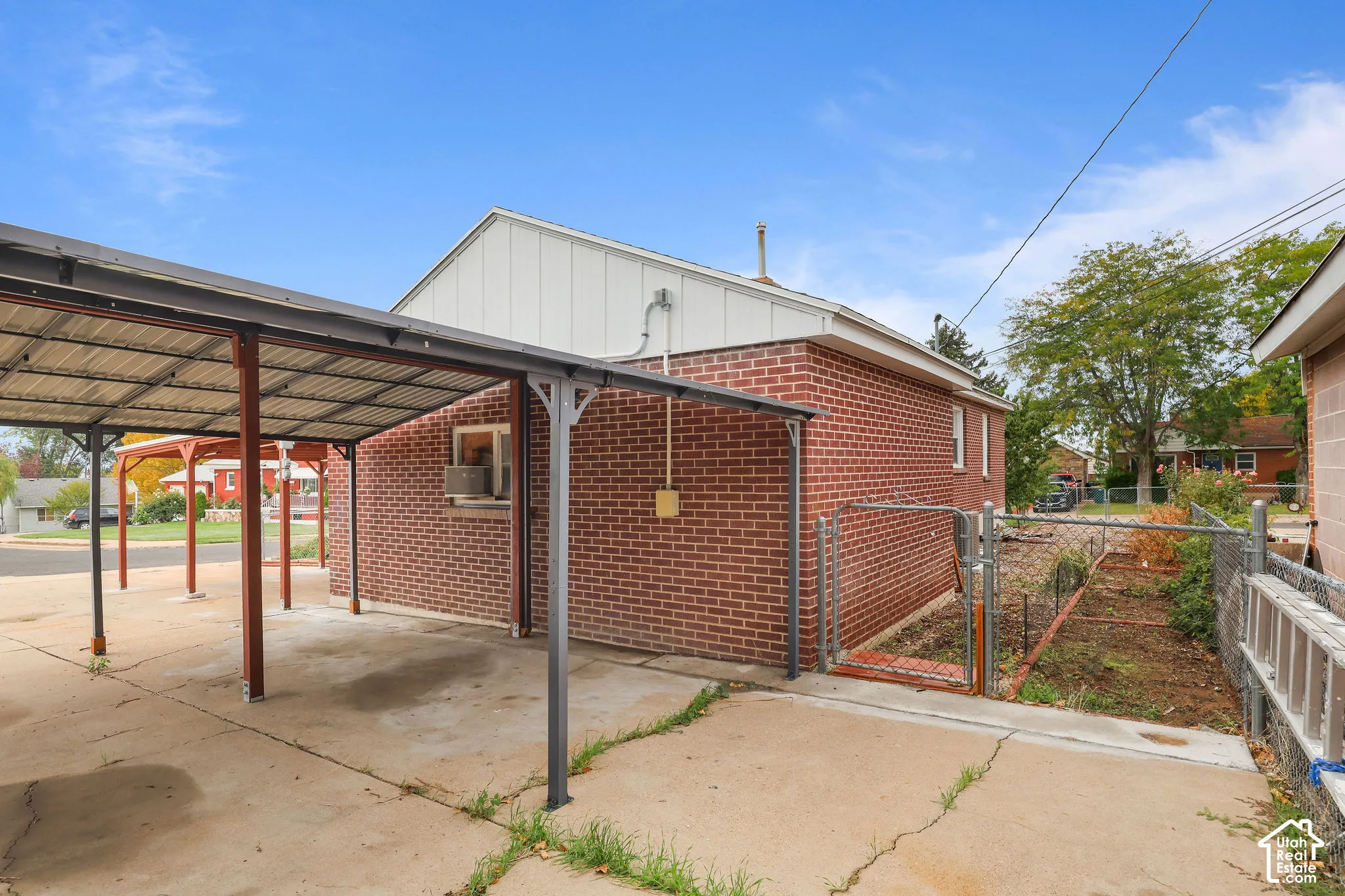 Brick exterior building with white siding, covered carport, concrete driveway, and chain-link fence